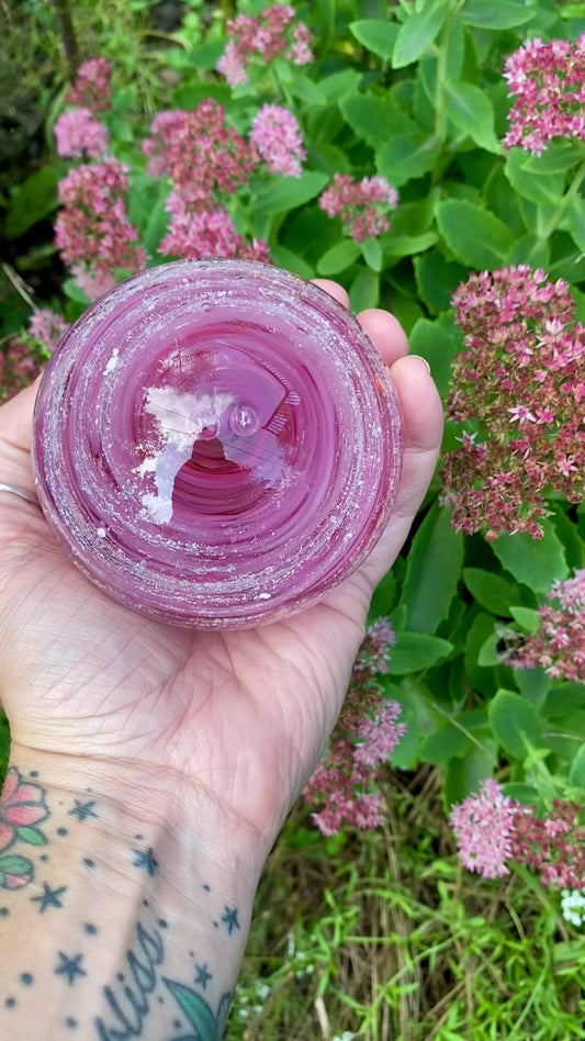 Hand holding a custom glass cremation keepsake in fuchsia and baby pink for size reference