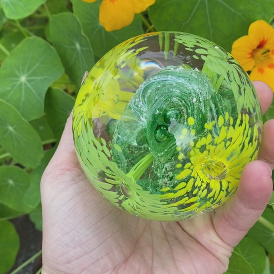 Custom glass memorial paperweight featuring four flower designs and vibrant swirling ashes with yellow and green