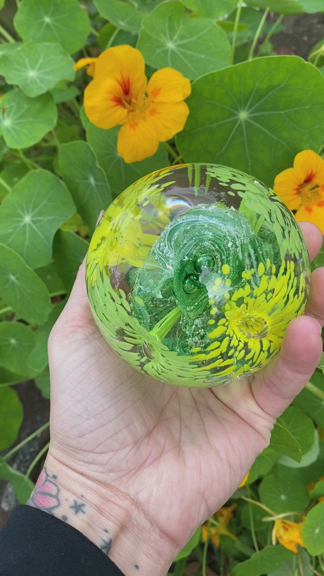 Custom glass memorial paperweight featuring four flower designs and vibrant swirling ashes with yellow and green